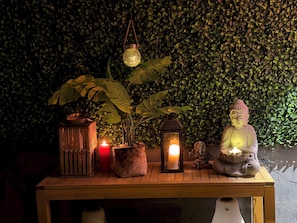 Ein Tisch mit Buddha-Statue, Kerzen und einer hängenden Laterne vor einer grünen Wand.