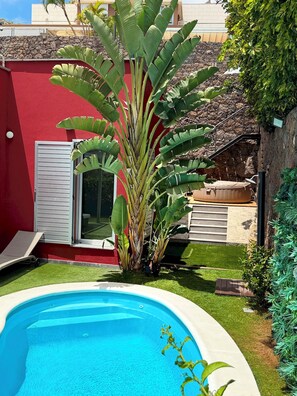 Ein Swimmingpool, umgeben von einer roten Mauer, einer großen Bananenpflanze und einem kleinen Garten.