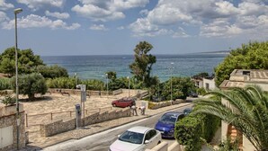 Uma rua costeira com carros estacionados, um banco e vista clara para o mar.