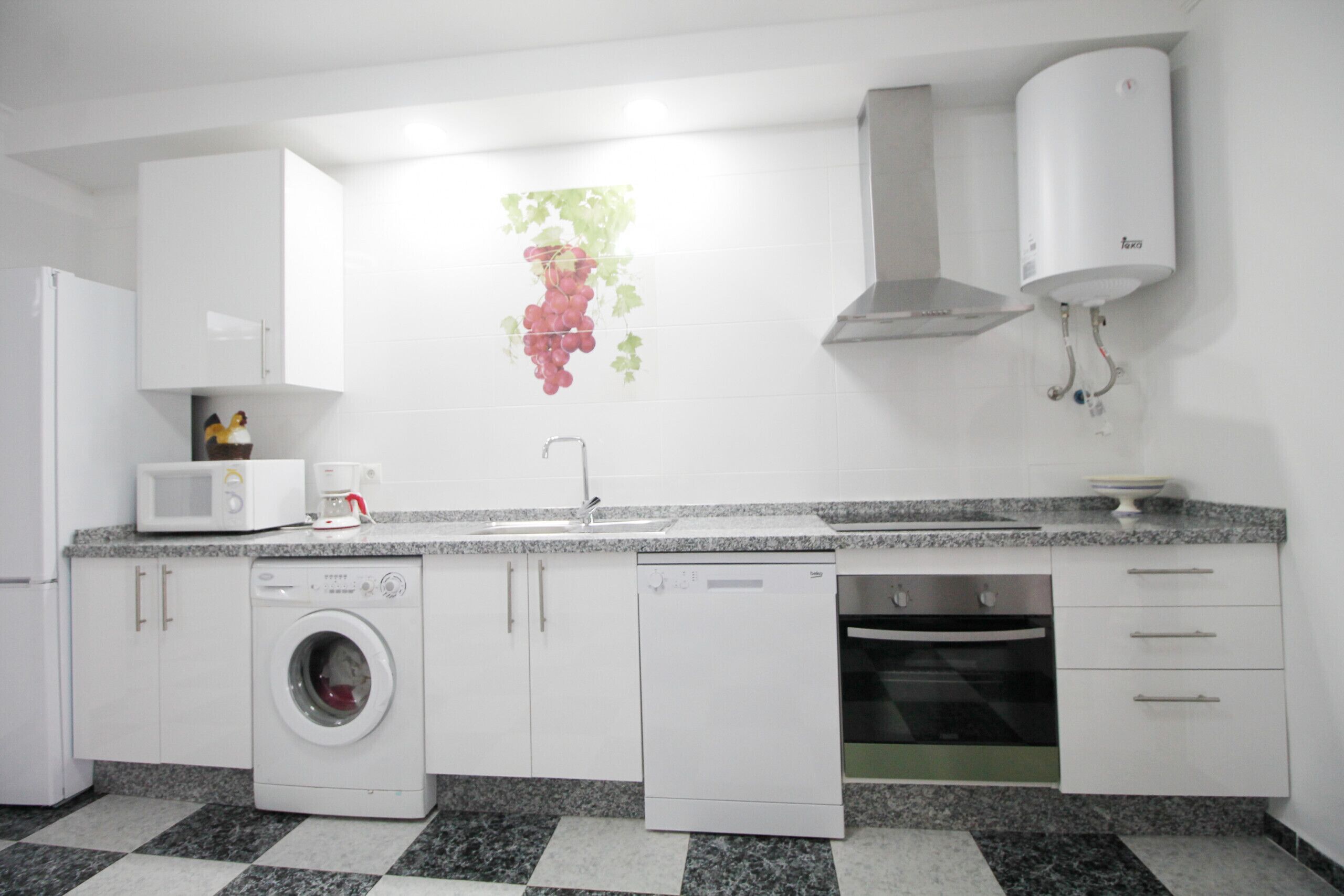 A modern kitchen with white cabinets, a washing machine, a dishwasher, a microwave, and a water heater.