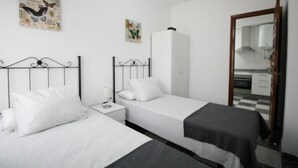 Ein Zimmer mit zwei Einzelbetten, einem weißen Kleiderschrank, einem Spiegel und einem kleinen Tisch mit einer Lampe.