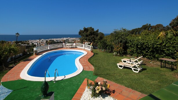 Ein Pool mit geschwungener Kante, umgeben von einem weißen Zaun, mit Blick auf das Meer im Hintergrund.