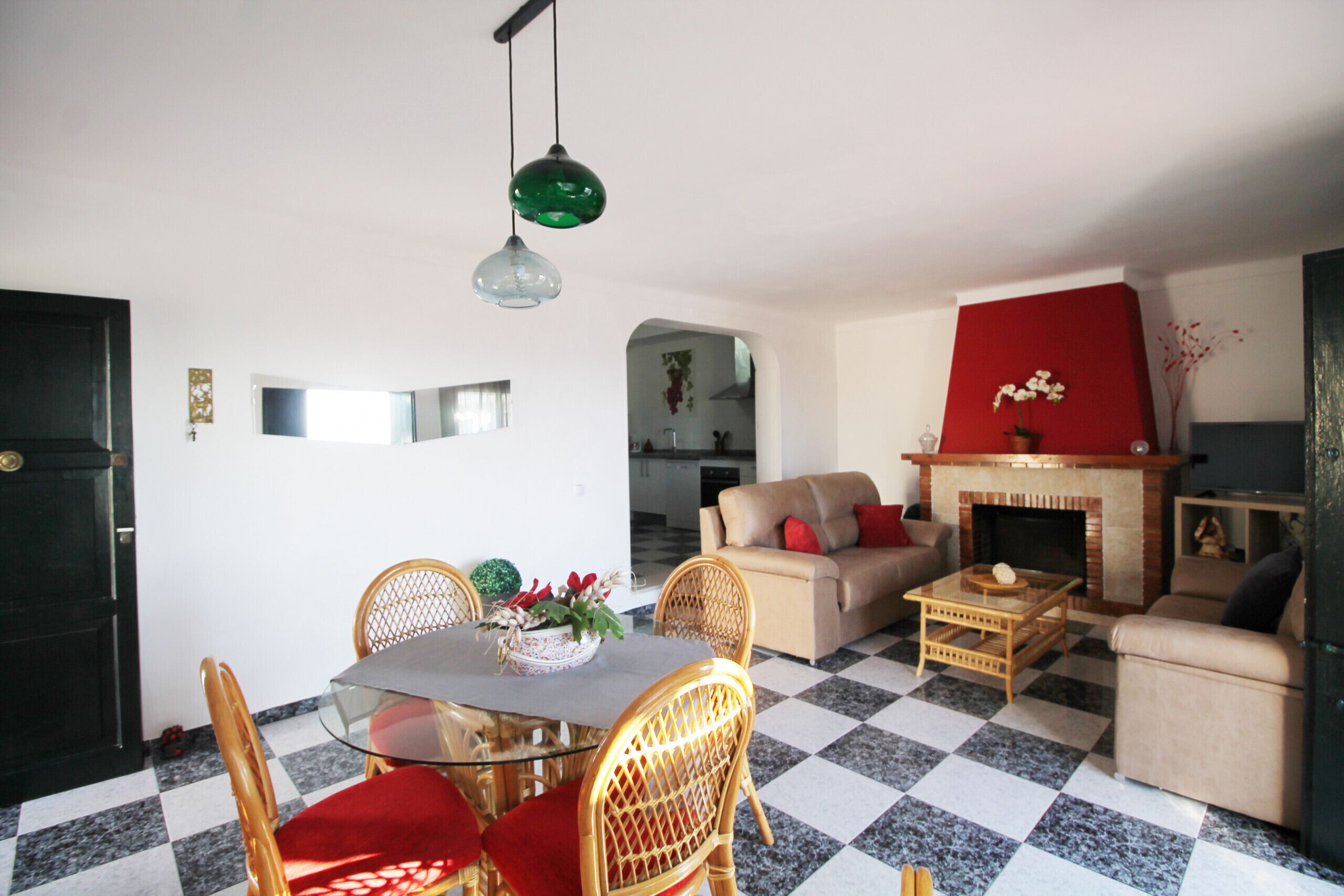 A living room with a checkered floor, a fireplace, and a dining area with wicker chairs and a glass table.