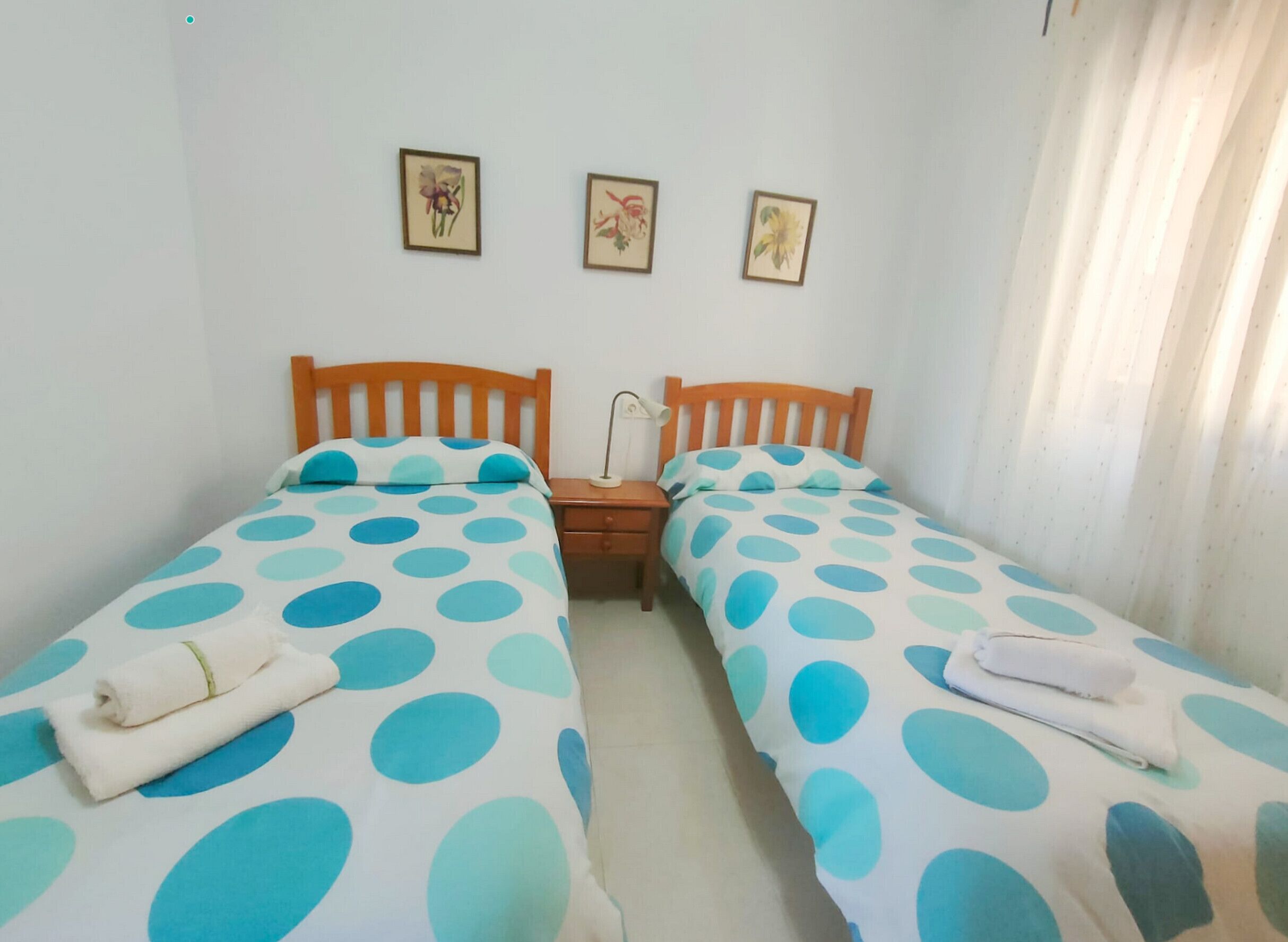 Une chambre avec deux lits, chacun doté d’une couette à pois, de têtes de lit en bois et d’une petite table de chevet avec une lampe. Trois tableaux encadrés ornent le mur.