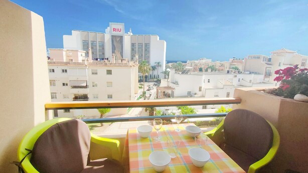 En balkon med spiseplads, stole og udsigt til bygninger, heriblandt en bygning med et 'RIU'-skilt.