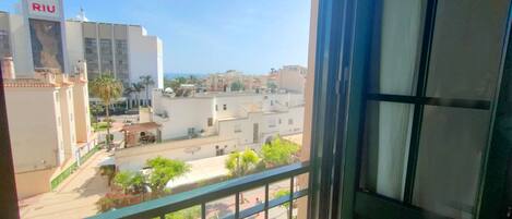 A view from a balcony with a clear sky, a building labeled "RIU" in the background, and a street with palm trees and other buildings.