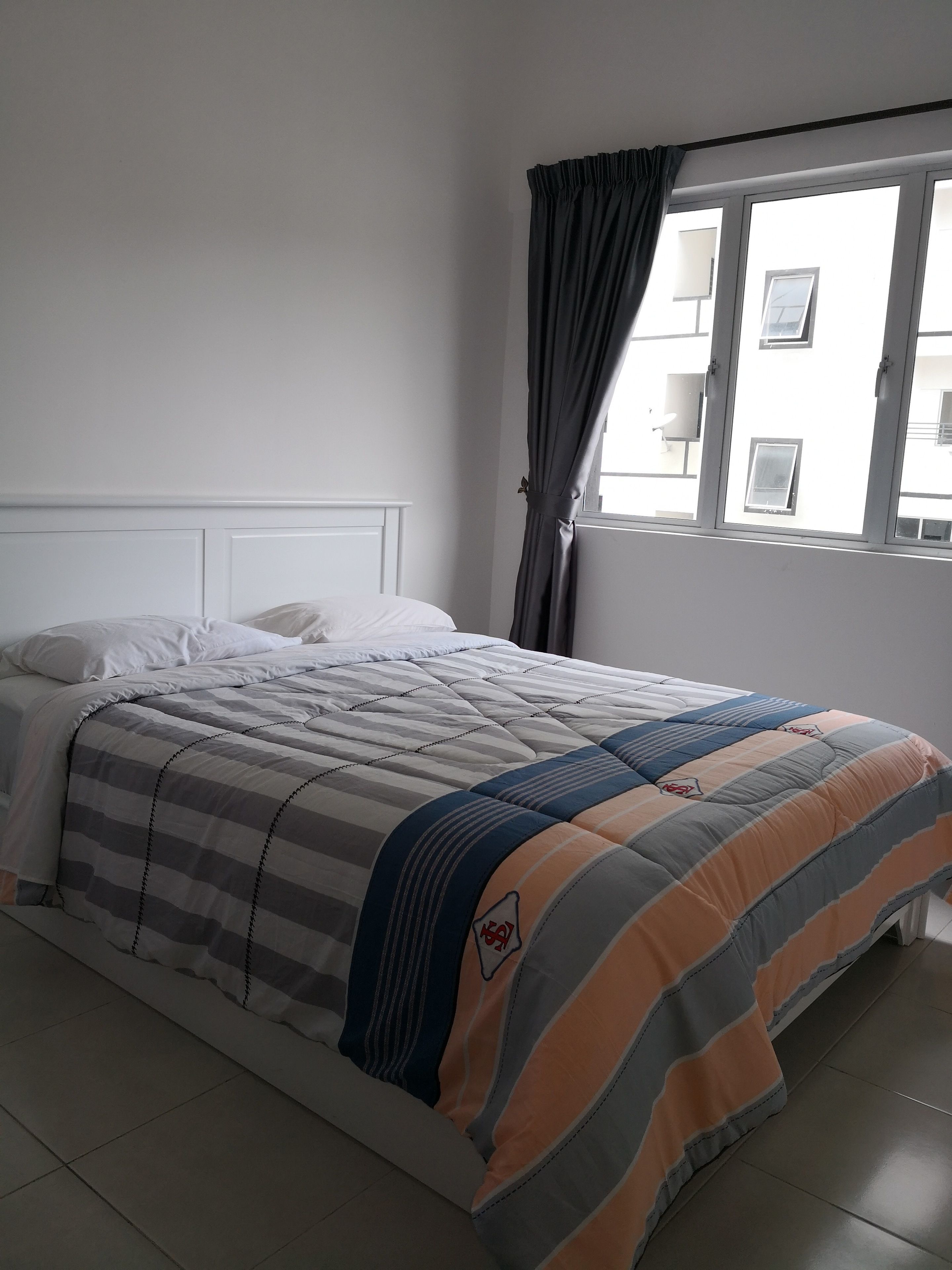 Une chambre à coucher avec un lit, une tête de lit blanche et une fenêtre avec des rideaux.
