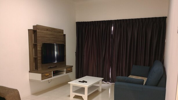 A living room with a TV mounted on a wooden wall, a white coffee table, a blue sofa, and a colorful rug. - Goodlife Paradise Cameron Jaya (Tanah Rata)