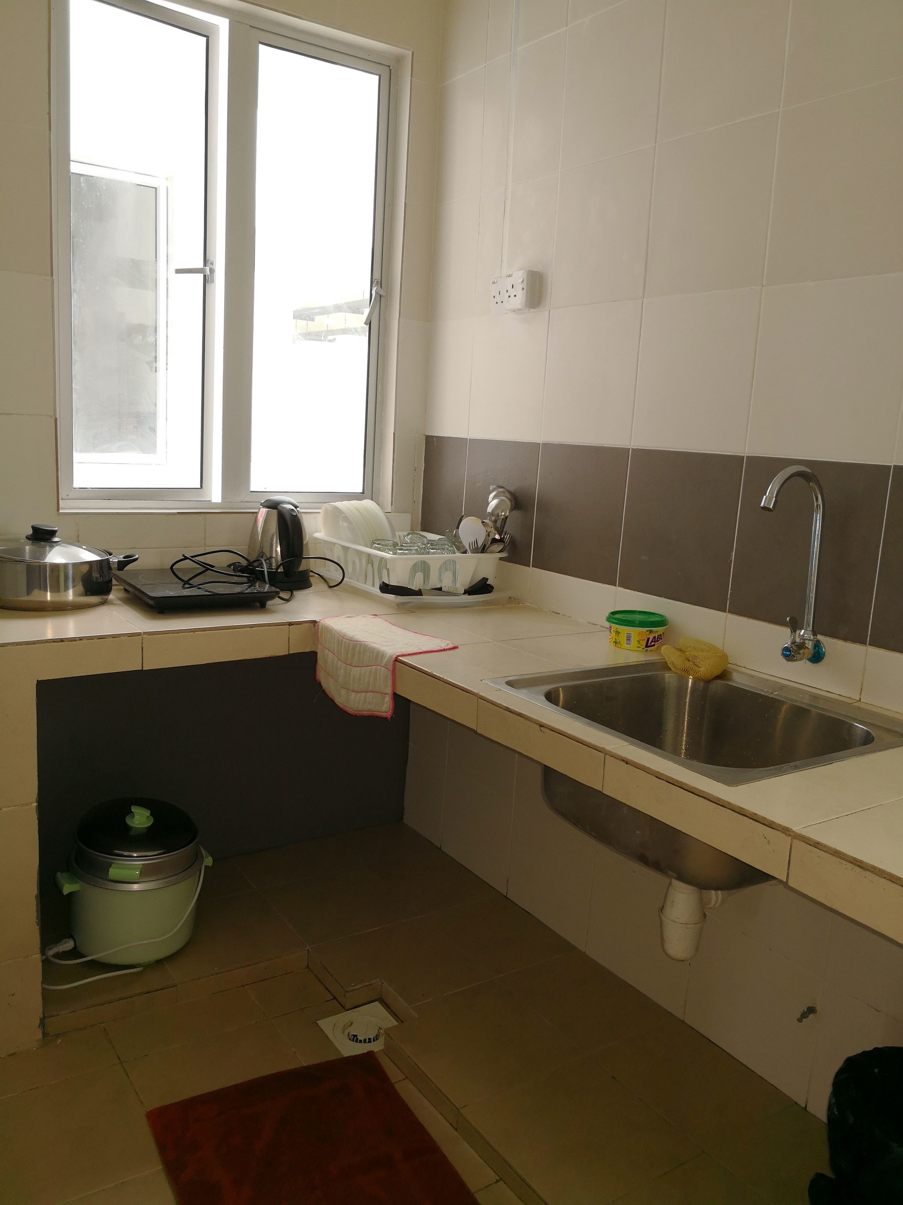 A kitchen with a window, a sink, a kettle, and a trash bin.