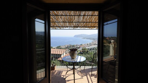 Un balcón con mesa y sillas, una planta en maceta y vistas al mar y edificios a lo lejos.
