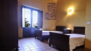 Un dormitorio con dos camas, un armario de madera, una pared de piedra y una ventana con vistas a árboles.