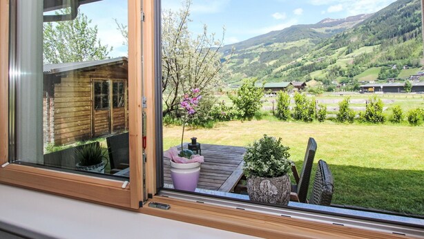 A view from a window of a wooden cabin with a patio area, a small garden, and a mountainous landscape in the background. - Nice apartment for 4 guests with WIFI, TV and patio (Helfenstein)