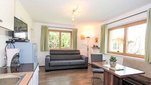 A compact living space with a kitchenette, a sofa, a dining table, and large windows. - Nice apartment for 4 guests with WIFI, TV and patio (Helfenstein)