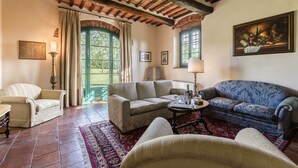 Un salon chaleureux avec une cheminée, des sièges confortables et une vue sur l’extérieur grâce à de grandes fenêtres.