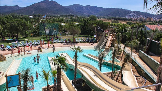A water park with multiple slides and a swimming pool, surrounded by palm trees and mountains in the background. - Amazing apartment on the seafront in Roses Inmosantos Oasis D4 (Rosas / Roses)