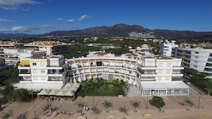 A multi-story building with a curved facade, surrounded by greenery and a mountainous backdrop. - Amazing apartment on the seafront in Roses Inmosantos Oasis D4 (Rosas / Roses)