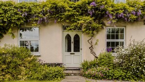 A building with a white door, arched windows, and a garden with various plants and flowers.