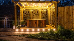 A wooden spa structure with a hot tub, surrounded by a decorative fence and string lights.