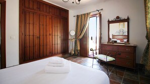 Un dormitorio con un amplio armario de madera, una cama con ropa blanca, un aparador, un espejo y una lámpara de araña.