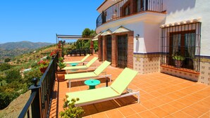 Una terraza con tumbonas y plantas en macetas, con vistas a un paisaje montañoso.