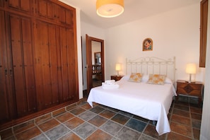 A bedroom with a large wooden wardrobe, a bed with white bedding, two bedside tables with lamps, and a small painting on the wall.