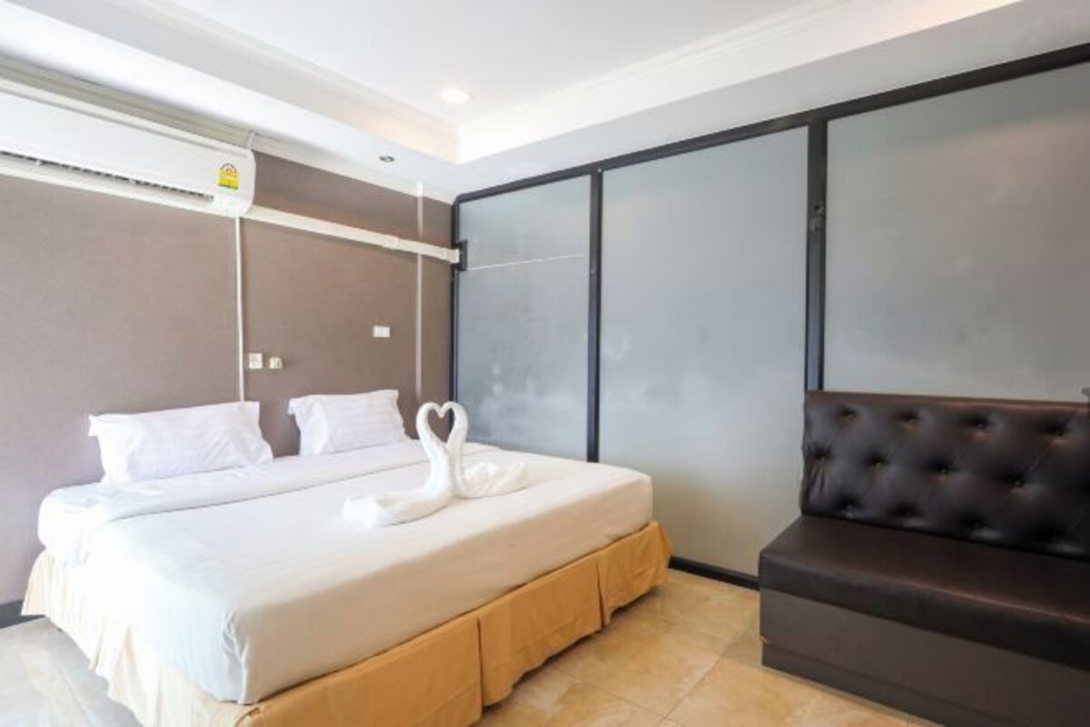 Una habitación de hotel con una cama grande, un banco tapizado negro y un aire acondicionado instalado en la pared.
