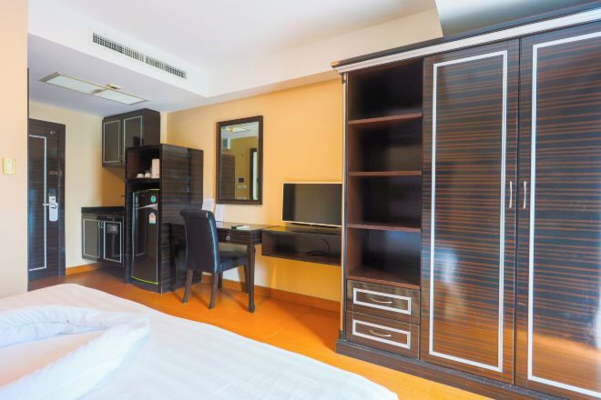 Habitación de hotel con cama, escritorio con silla, televisor y armario.