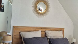 A bedroom with a wooden headboard, two pillows, a bedside lamp, and a mirror with a sunburst frame on the wall. - Apartment/ flat - Concarneau (Concarneau)