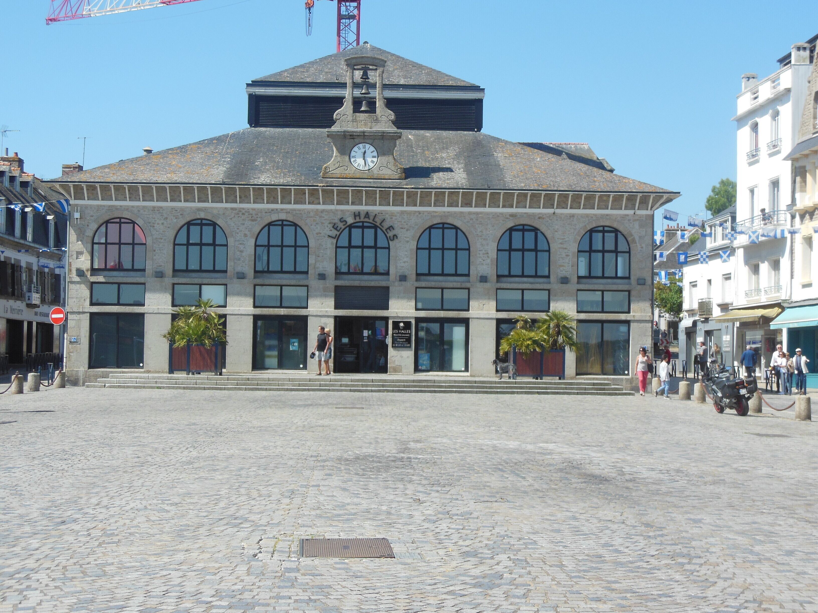 Un bâtiment historique doté d’une tour horlogée, de grandes fenêtres en arc de cercle et d’une place pavée.