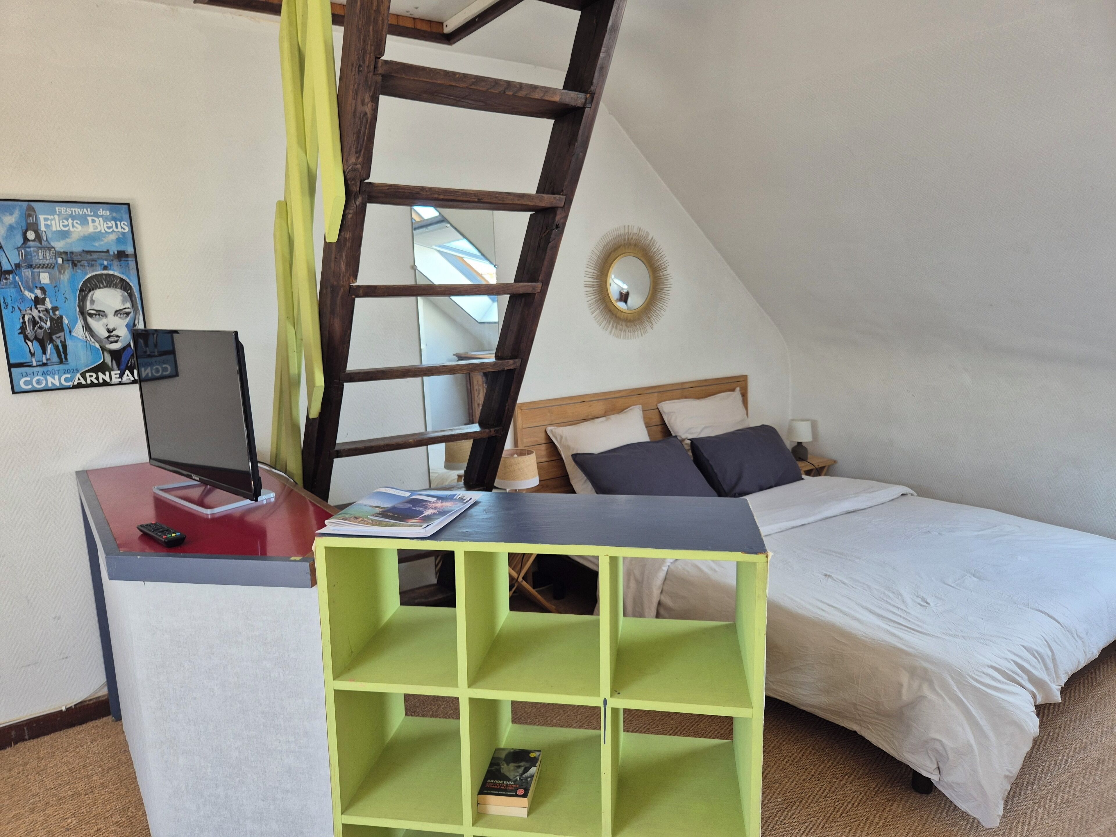 A bedroom with a bed, a desk with a computer, a bookshelf, a ladder, and a poster on the wall.