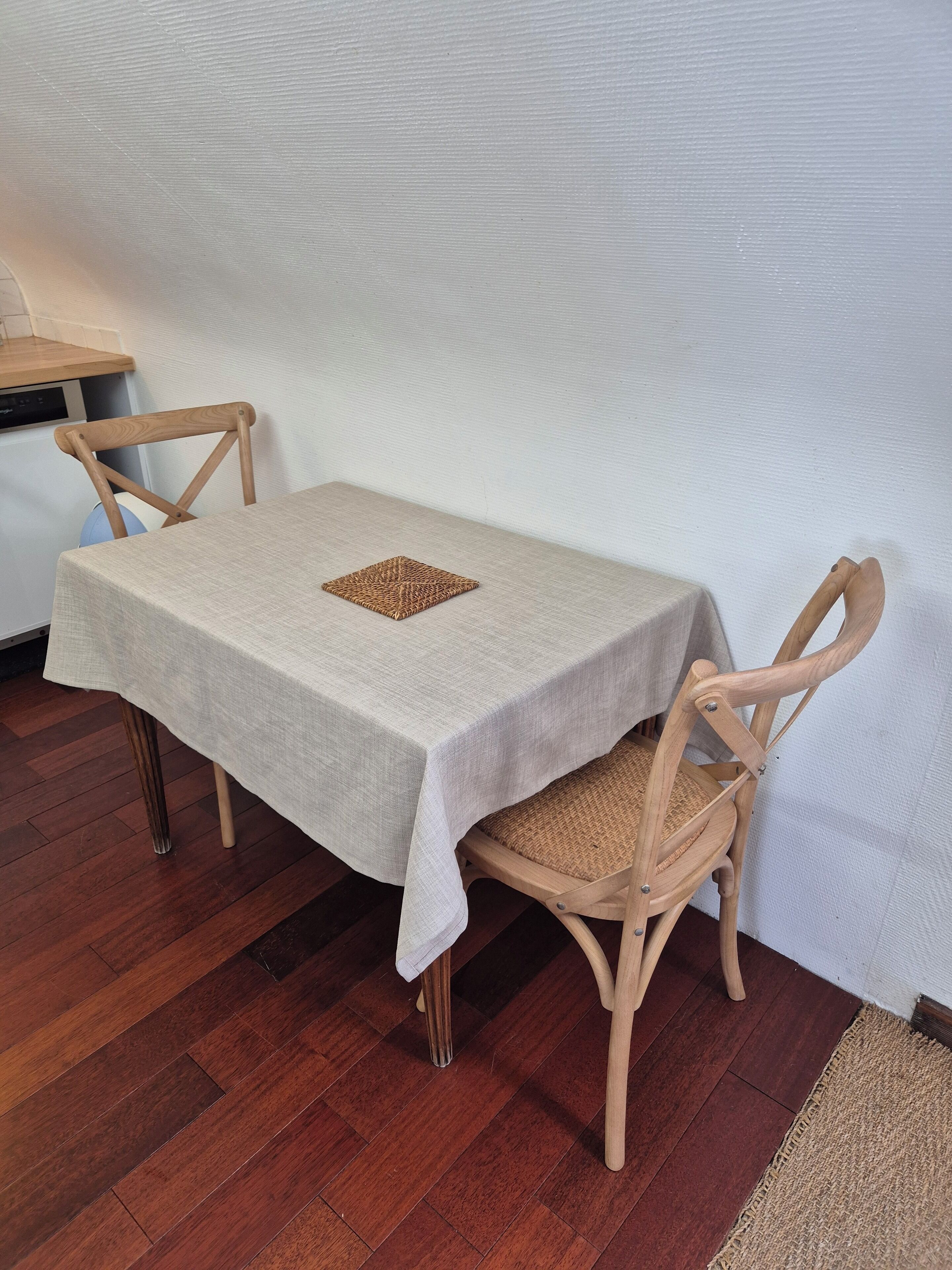 A small dining table with a white tablecloth, two wooden chairs, and a woven placemat.