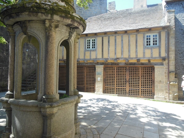 A stone structure with arches, a building with wooden shutters, and a paved courtyard.