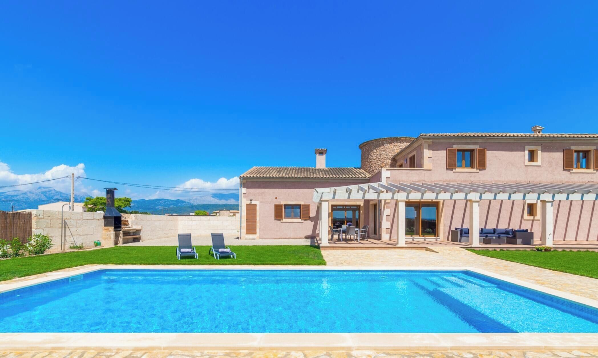 Una casa de dos pisos con piscina, mobiliario exterior y vista a las montañas.