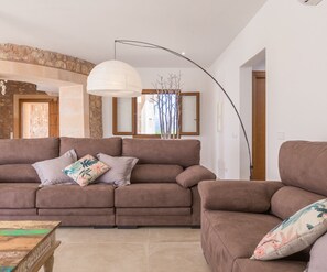 Una sala de estar con un sofá marrón, una lámpara colgante blanca y vista al mar a través de una ventana.