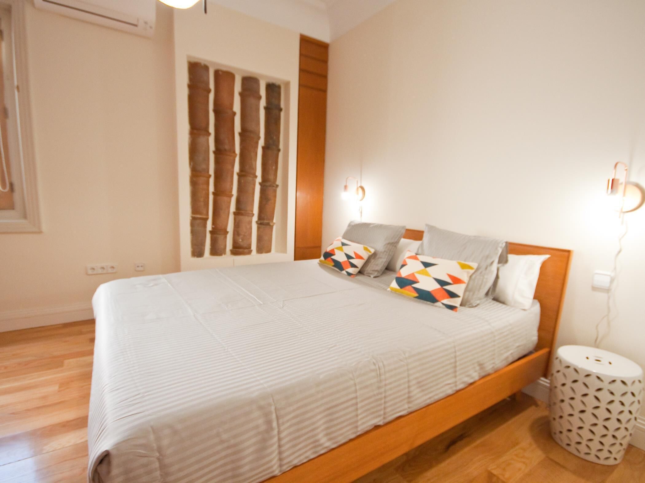 Een slaapkamer met een houten bedframe, een witte spreidek en gekleurde kussens.