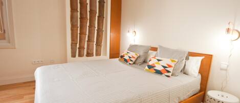 Een slaapkamer met een houten bedframe, een witte spreidek en gekleurde kussens.