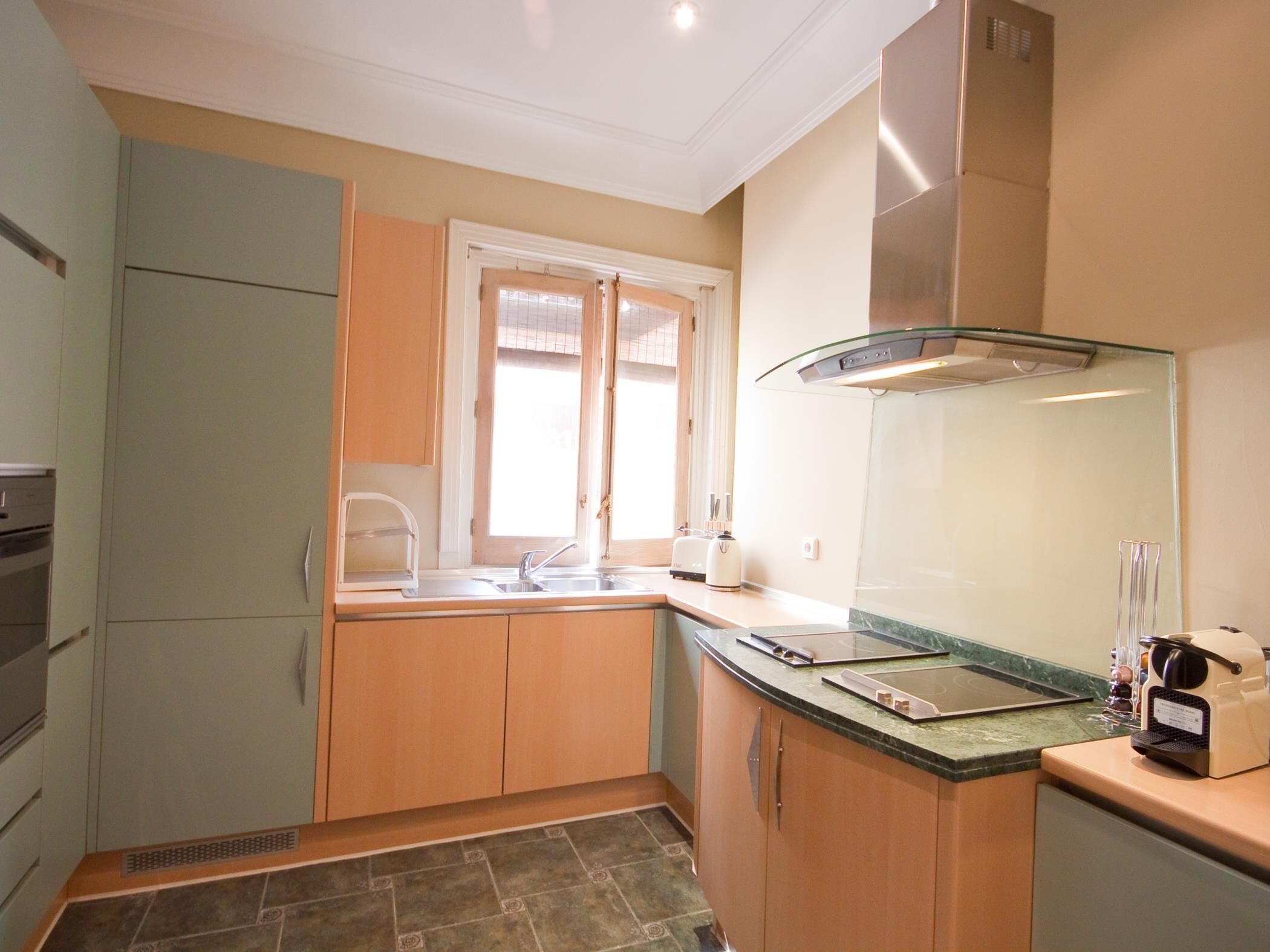 A compact kitchen with wooden cabinets, a built-in oven, a sink, and a window.