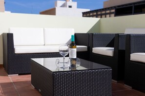 An outdoor seating area with a glass-top table, a bottle of wine, and a glass.