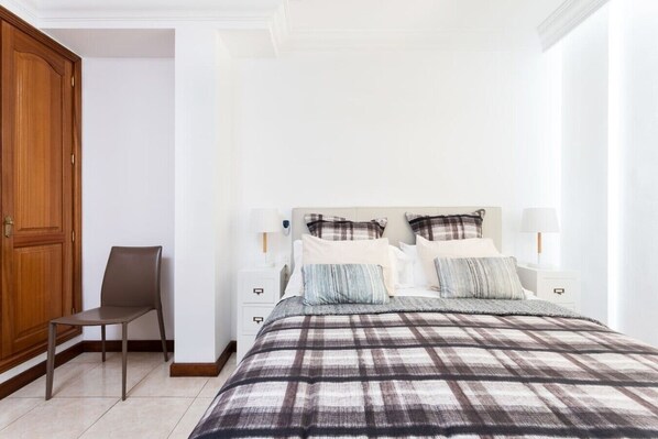 A bedroom with a bed, bedside tables, a chair, and a wooden door.