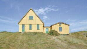 A yellow two-story house with a triangular roof and green windows, situated on a grassy hill. - 4 bedroom beautiful home in Frøstrup (Frøstrup)