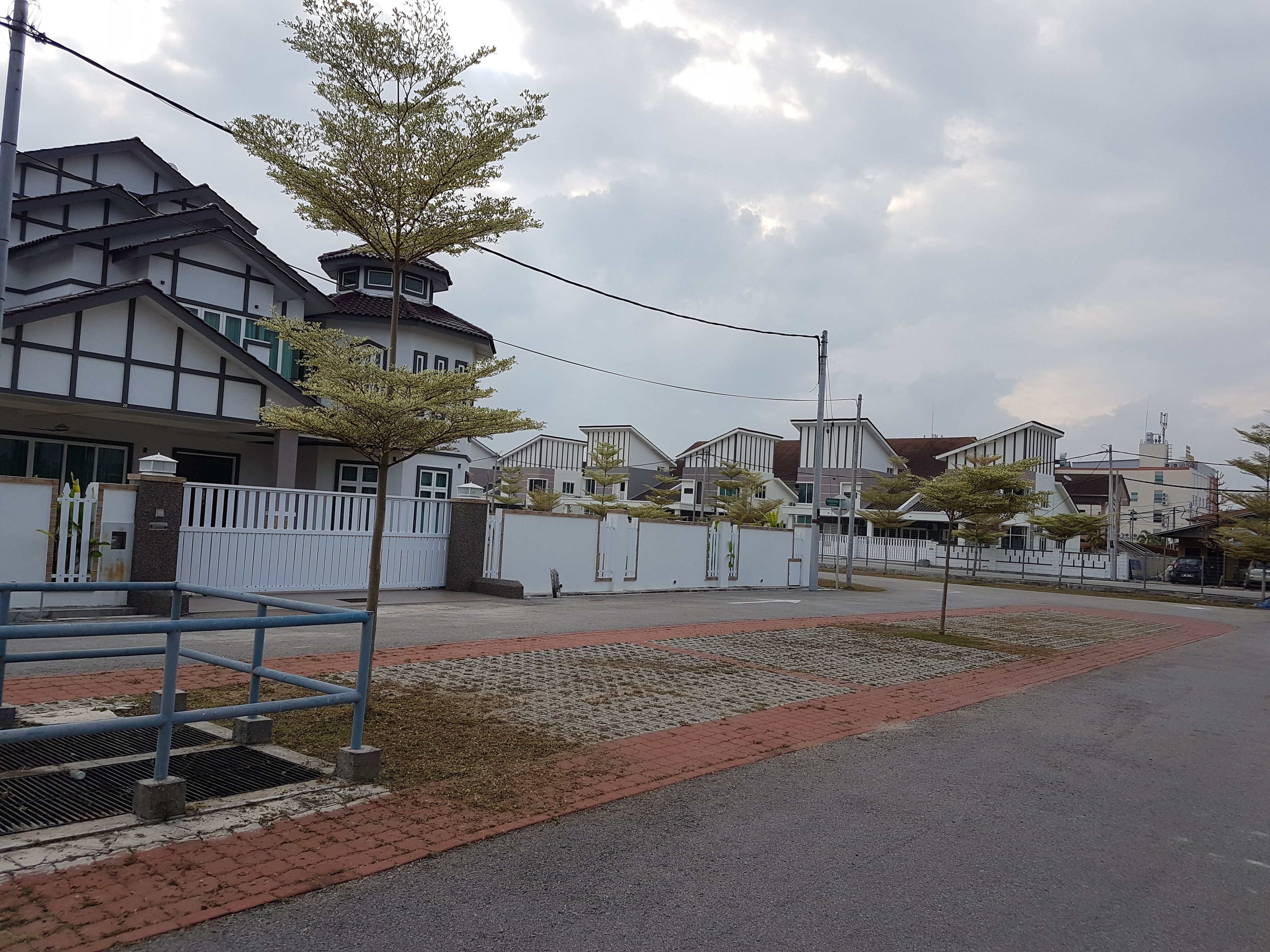 Una calle residencial con casas, un acceso con reja y una acera pavimentada.