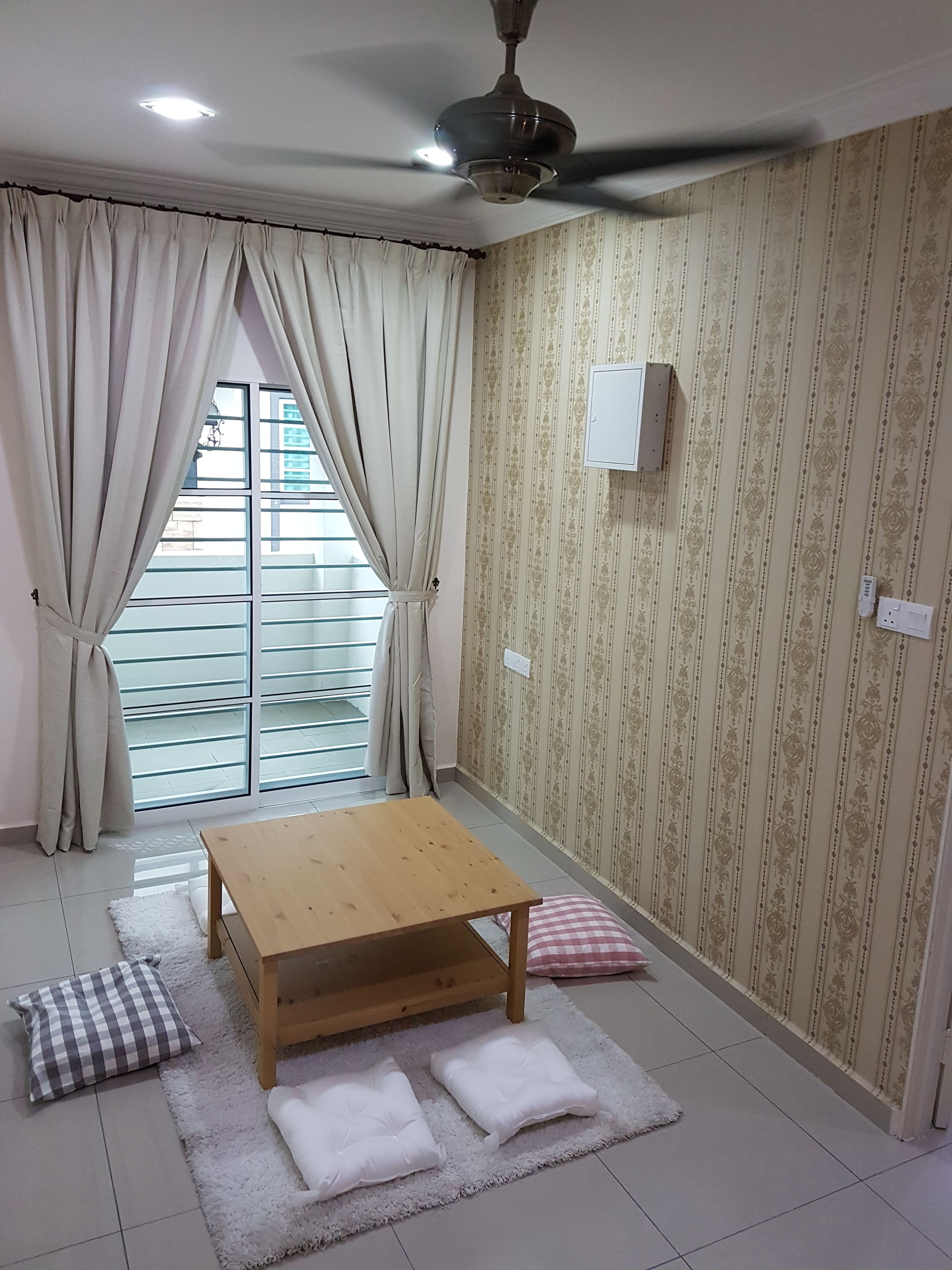 A room with a wooden table, two white cushions, a checkered pillow, a ceiling fan, and a window with curtains.