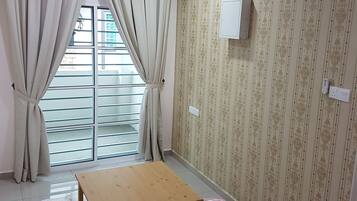 A room with a wooden table, two white cushions, a checkered pillow, a ceiling fan, and a window with curtains.
