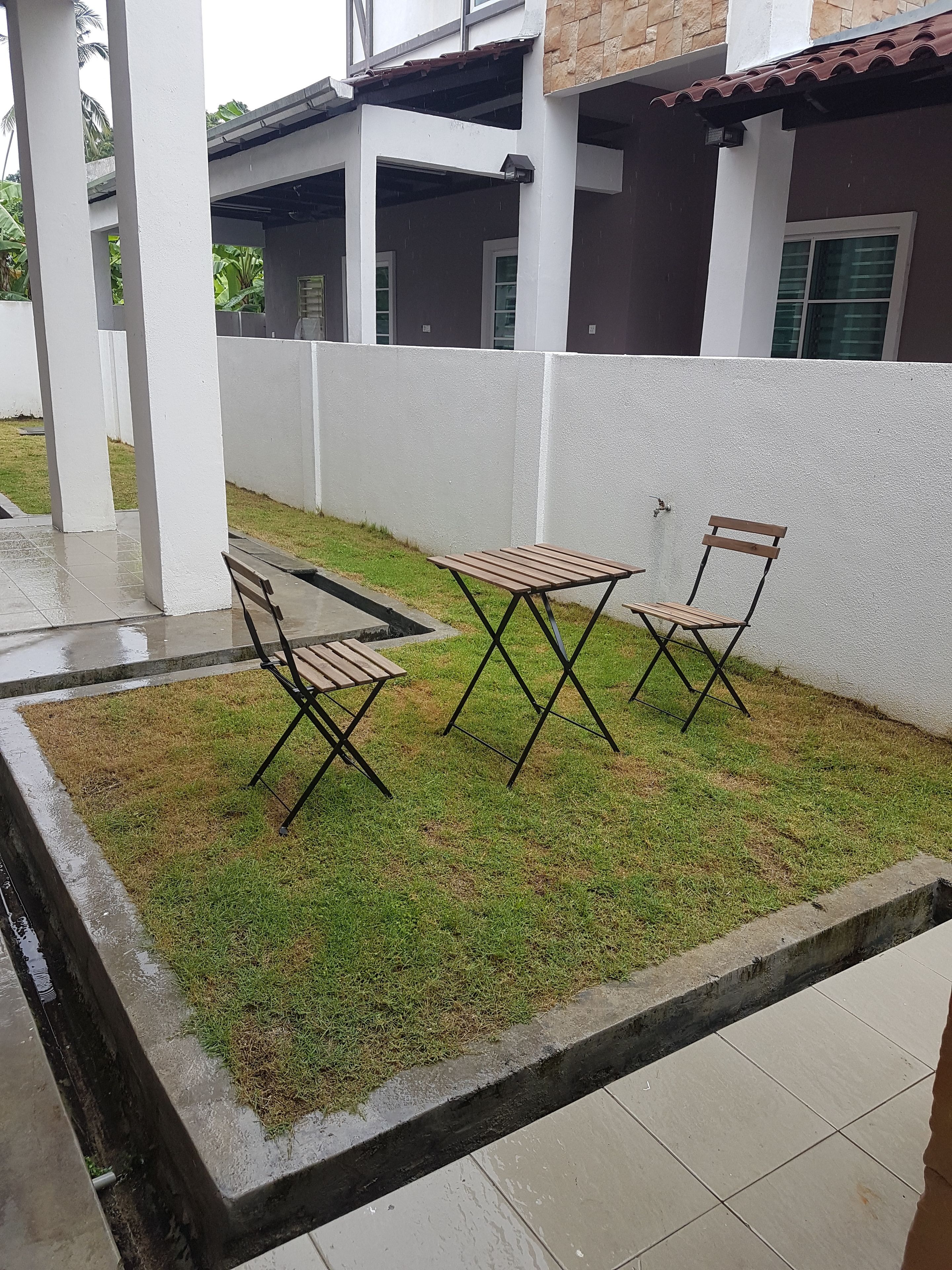 A patio area with a table and two chairs, surrounded by a low white wall and a grassy area.