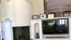 Ein Wohnzimmer mit Kamin, einem Fernseher auf einem weißen Schrank und einer Steinschale auf dem Boden.