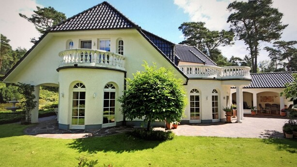 Ein großes, helles Haus mit Balkon, gepflegtem Rasen und Garten.