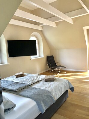 Une chambre à coucher avec un grand lit, un téléviseur à écran plat fixé au mur, une fenêtre et un fauteuil.