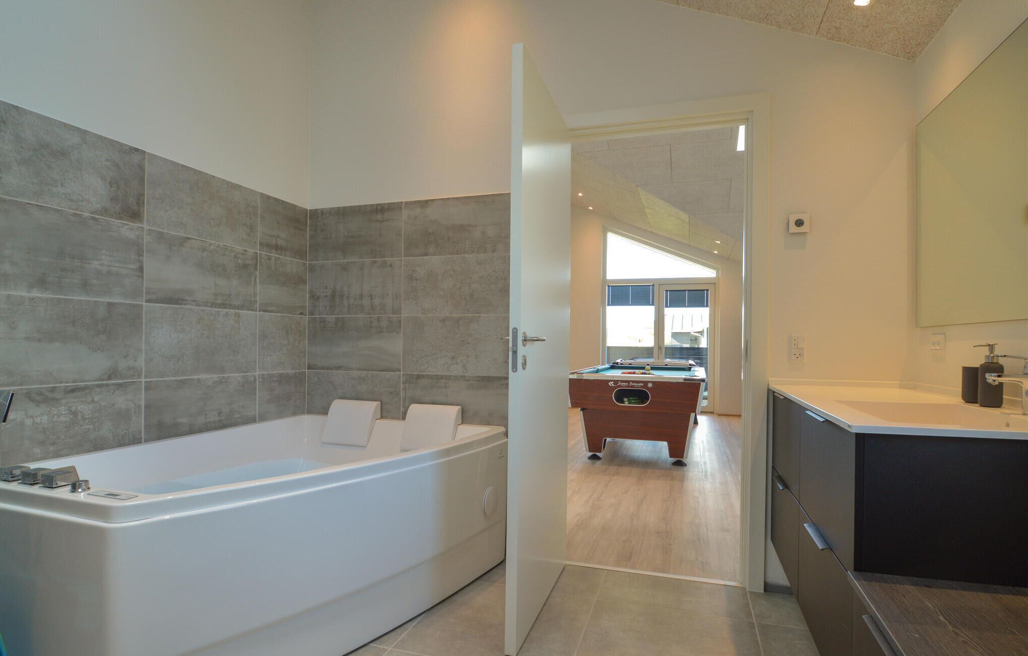 Un baño moderno con una bañera grande, zona de ducha separada y una mesa de billar en la habitación contigua.