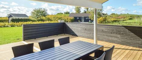 An outdoor patio with a wooden table and chairs, a bench, and a view of a house and garden.