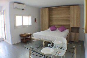 Un dormitorio moderno con una cama, una mesa de vidrio con vajilla y una ventana.